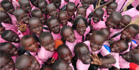 A crowd of children in pink shirts smiling up at at the camera